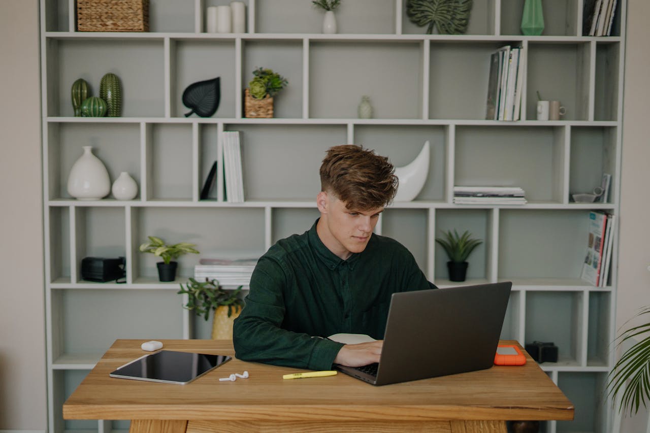 Services-01 A man focused on using his laptop at a stylish home office desk with shelves.