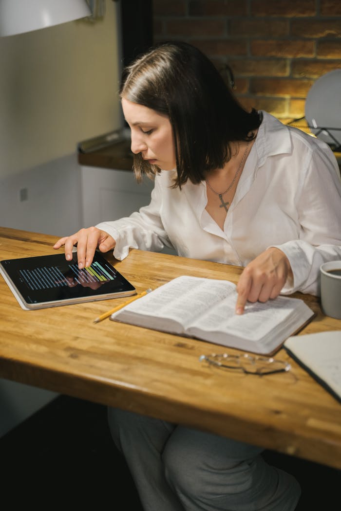 Services-03 A woman studies the Bible at a wooden table, combining printed and digital texts.